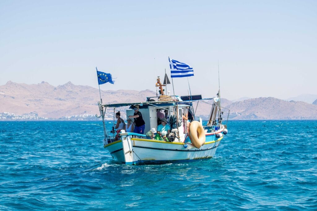 The Captain Tasos with guests on board, Greek and EU flags flying, Kos coast behind