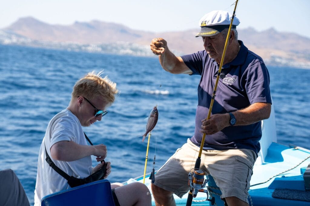 Crew helping a young guest reel in a fish on a Kos fishing trip